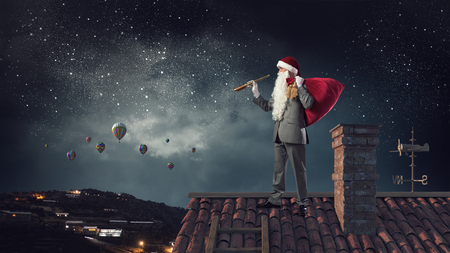 Businessman in Santa hat on house roof looking in spyglassの写真素材