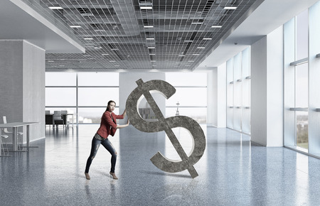 Young woman in office pushing stone dollar signの写真素材