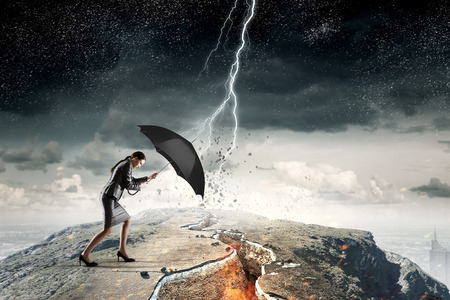 Young determined businesswoman with umbrella walking against strong windの写真素材