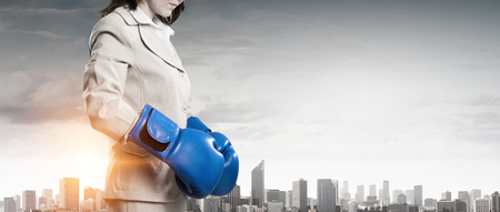 Businesswoman in boxing gloves against city backgroundの写真素材