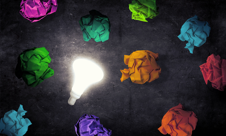 Glowing light bulb and paper balls on dark backgroundの写真素材