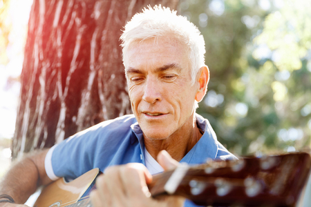 Handsome senior man playing guitar in summer parkの写真素材