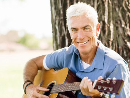 Handsome senior man playing guitar in summer parkの写真素材