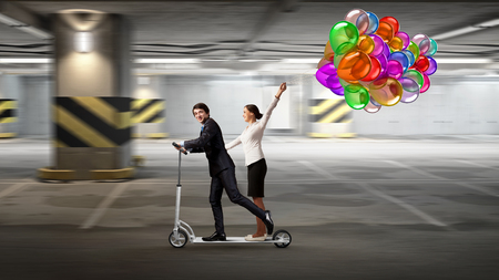 Young cheeful businesspeople riding scooter in office. Mixed mediaの写真素材