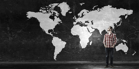 Young student guy in glasses and world map on wallの写真素材