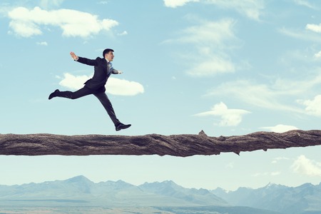 Young successful businessman running on log above gap. Risk and challenge conceptの写真素材