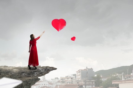 Beautiful woman in red dress reaching hand in gestureの写真素材