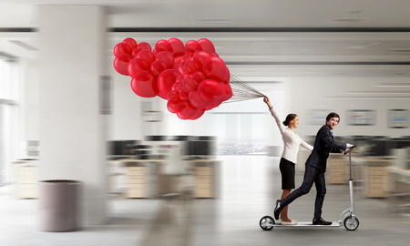 Young cheeful businesspeople riding scooter in office. Mixed mediaの写真素材