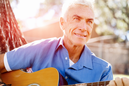 Handsome senior man playing guitar in summer parkの写真素材