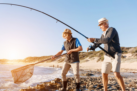 Senior man fishing with his teenage grandson at seasideの写真素材
