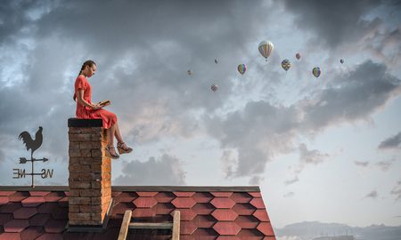 Girl sitting on roof chimney and reading bookの写真素材