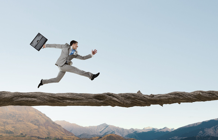 Young successful businessman running on log above gap. Risk and challenge conceptの写真素材