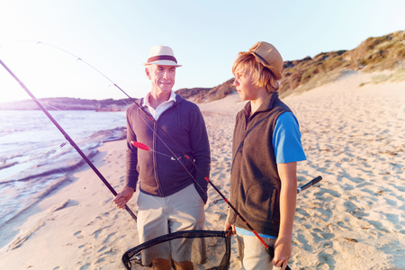 Senior man fishing with his teenage grandson at seasideの写真素材