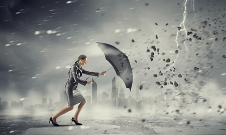 Young determined businesswoman with umbrella walking against strong windの写真素材