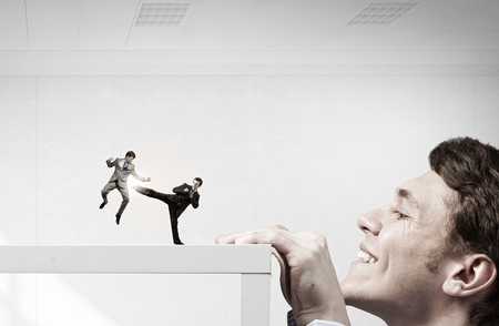 Businessman peeping from under table at people fighting with each other. Mixed mediaの写真素材