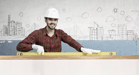 Young handsome man in hardhat with measure level