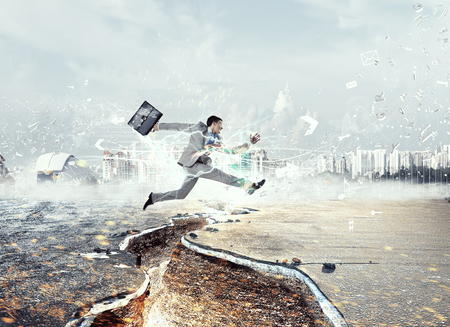 Determined businessman jumping over crack in asphalt roadの写真素材