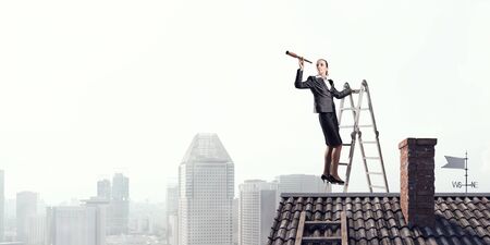 Businesswoman climbing ladder and looking through spyglassの写真素材