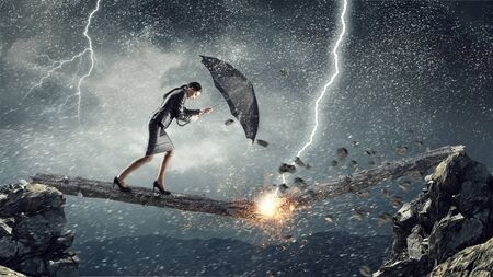 Young determined businesswoman with umbrella walking against strong wind