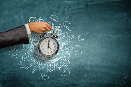 Hand holding vintage alarm clock over chalkboard backgroundの写真素材