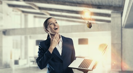 Pensive young businesswoman in interior with laptop in hands. Mixed mediaの写真素材