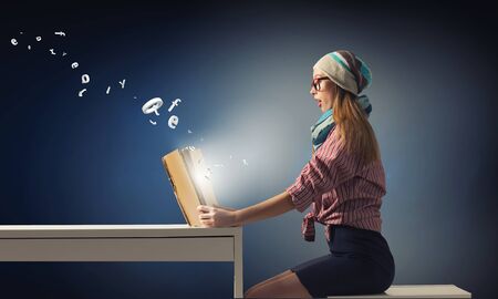 Attractive hipster girl sitting at desk and reading bookの写真素材