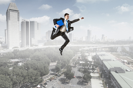 Active businessman jumping high in sky against cityscape backgroundの写真素材