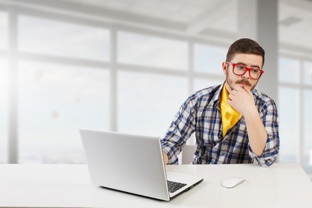 Young man in glasses and checked shirt working on laptop. Mixed media