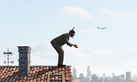 Businessman in suit and diving mask jumping from house roofの写真素材