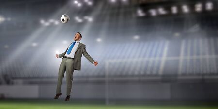 Businessman at soccer field taking ball on his head. Mixed mediaの写真素材