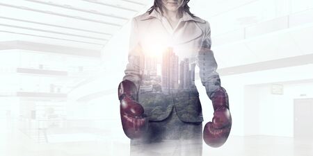 Businesswoman in boxing gloves against cityscape backgroundの写真素材