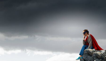 Young attractive woman in mask and red cape on rock topの写真素材