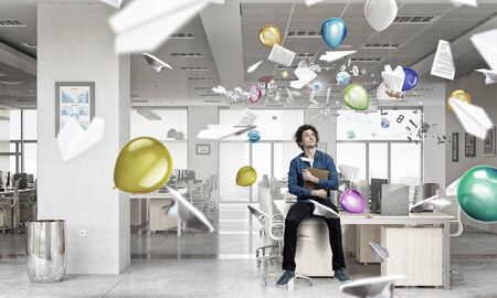 Young man in office sitting on table with book in hands. Mixed mediaの写真素材