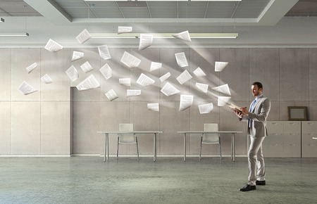Young pretty businessman with notepad in hands and papers flying out. Mixed mediaの写真素材