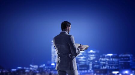 Young businessman with papers in hands against night city backgroundの写真素材
