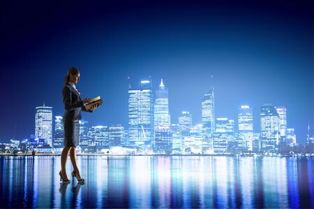Young businesswoman with papers in hands against night city backgroundの写真素材