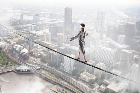 Businesswoman with blindfolder on eyes balancing on the ropeの写真素材