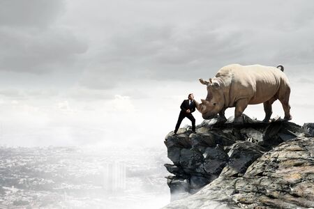 Businessman making effort to move huge rhinoの写真素材
