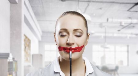 Portrait of young businesswoman painting her lips in red color. Mixed mediaの写真素材