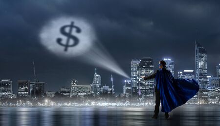 Young businessman in mask and cape and dollar sign glowing in skyの写真素材