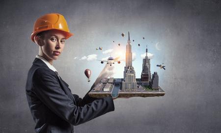 Young woman engineer in helmet and suit holding architecture pattern. Mixed mediaの写真素材