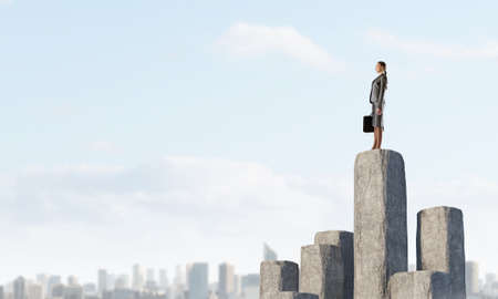 Businesswoman in suit with briefcase on stone column peak. Mixed mediaの写真素材