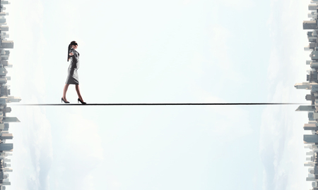 Businesswoman with blindfolder on eyes balancing on the ropeの写真素材