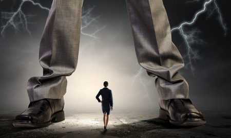 Little bussineswoman and giant boss legs as concept of powerの写真素材