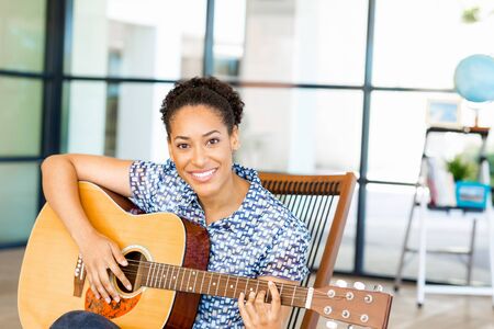 Portrait of smiling afro-american office worker sitting in offfice with guitar