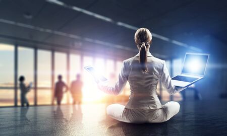 Young attractive woman sitting cross legged lotus yoga pose at office table. Mixed mediaの写真素材