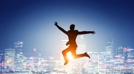 Silhouette of businessman jumping in air against modern cityscape. Mixed mediaの写真素材