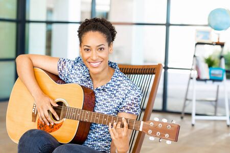 Portrait of smiling afro-american office worker sitting in offfice with guitar