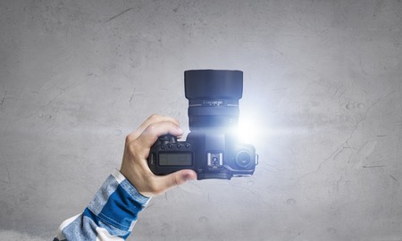Male hands holding photo camera on the dark wall backgroundの写真素材