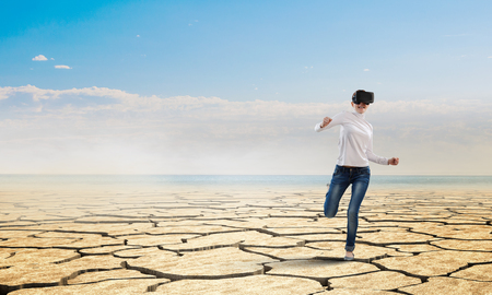Young woman wearing virtual helmet running in desert. Mixed mediaの写真素材
